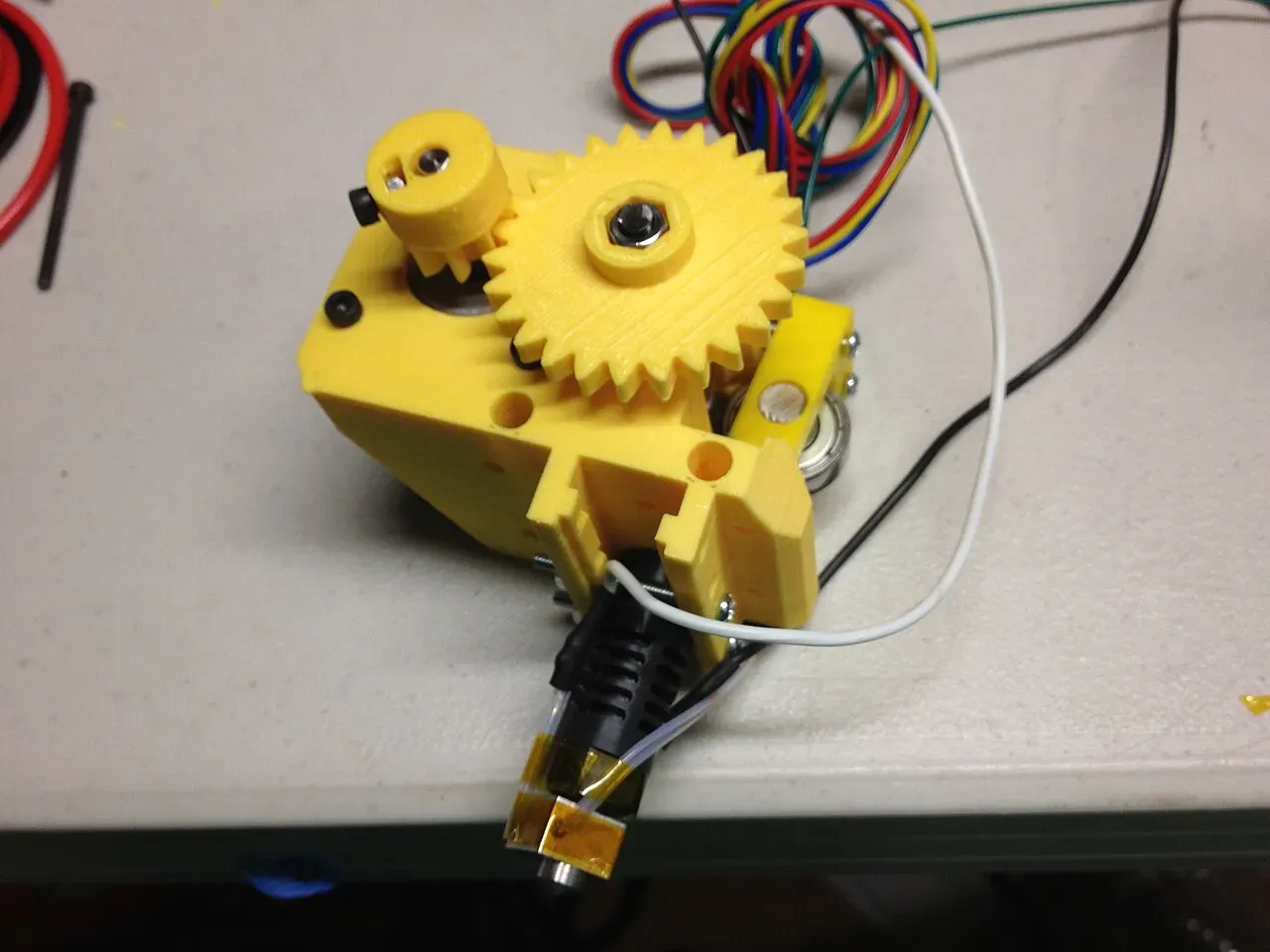 An assembled yellow extruder with drive gears and wiring