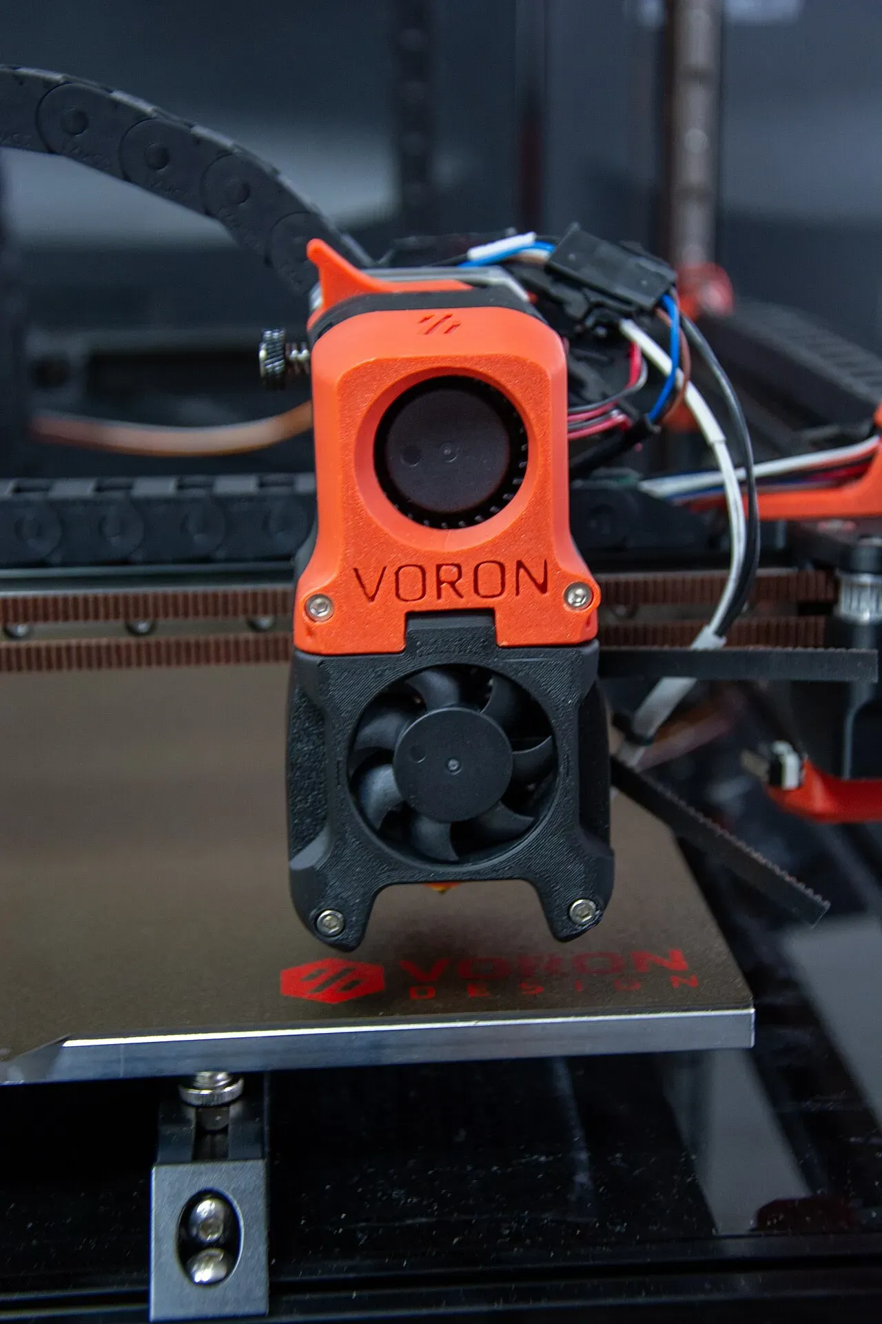 An orange Voron printer toolhead with its fans