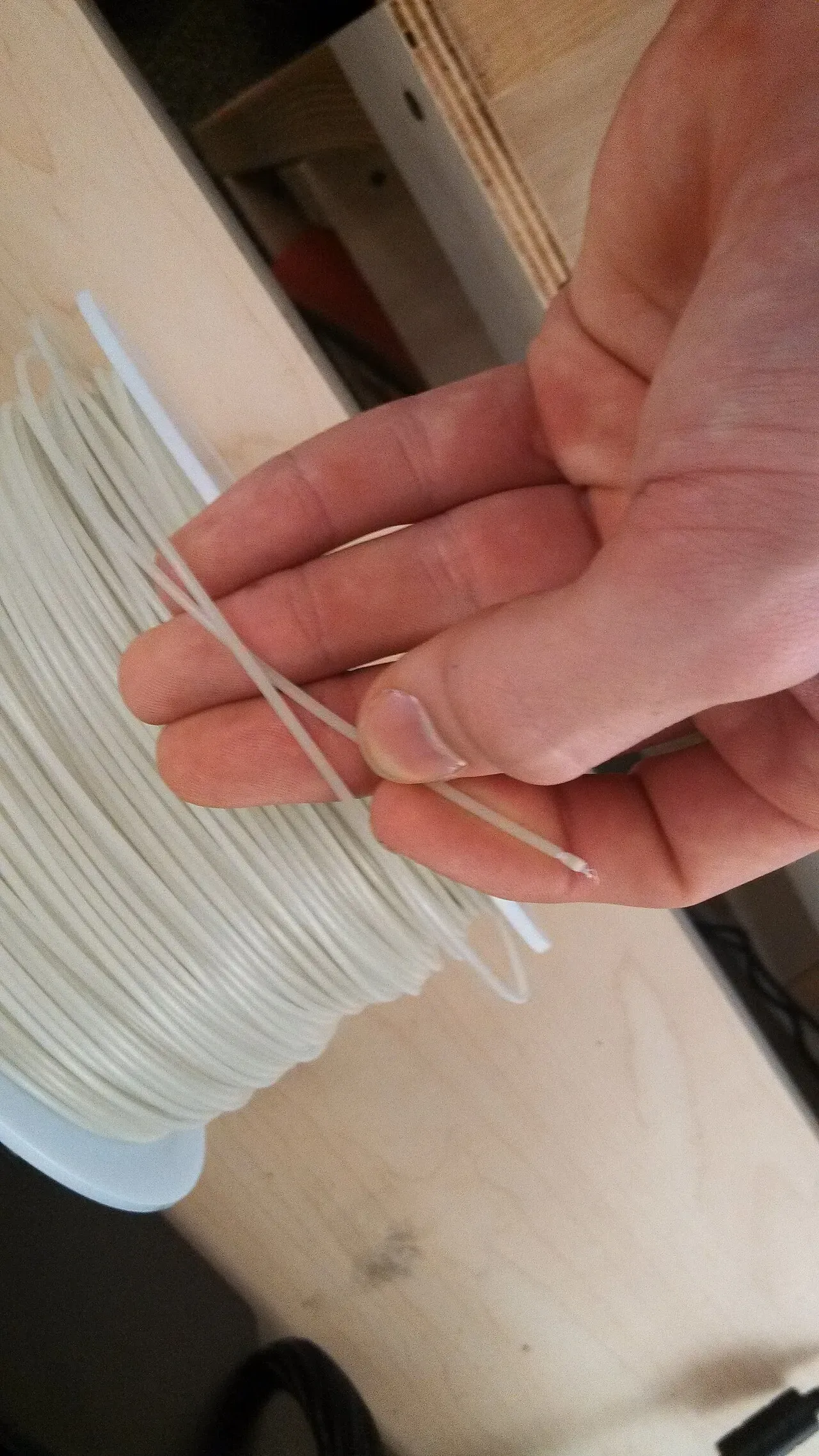 A hand holding filament that has crossed over itself on the spool