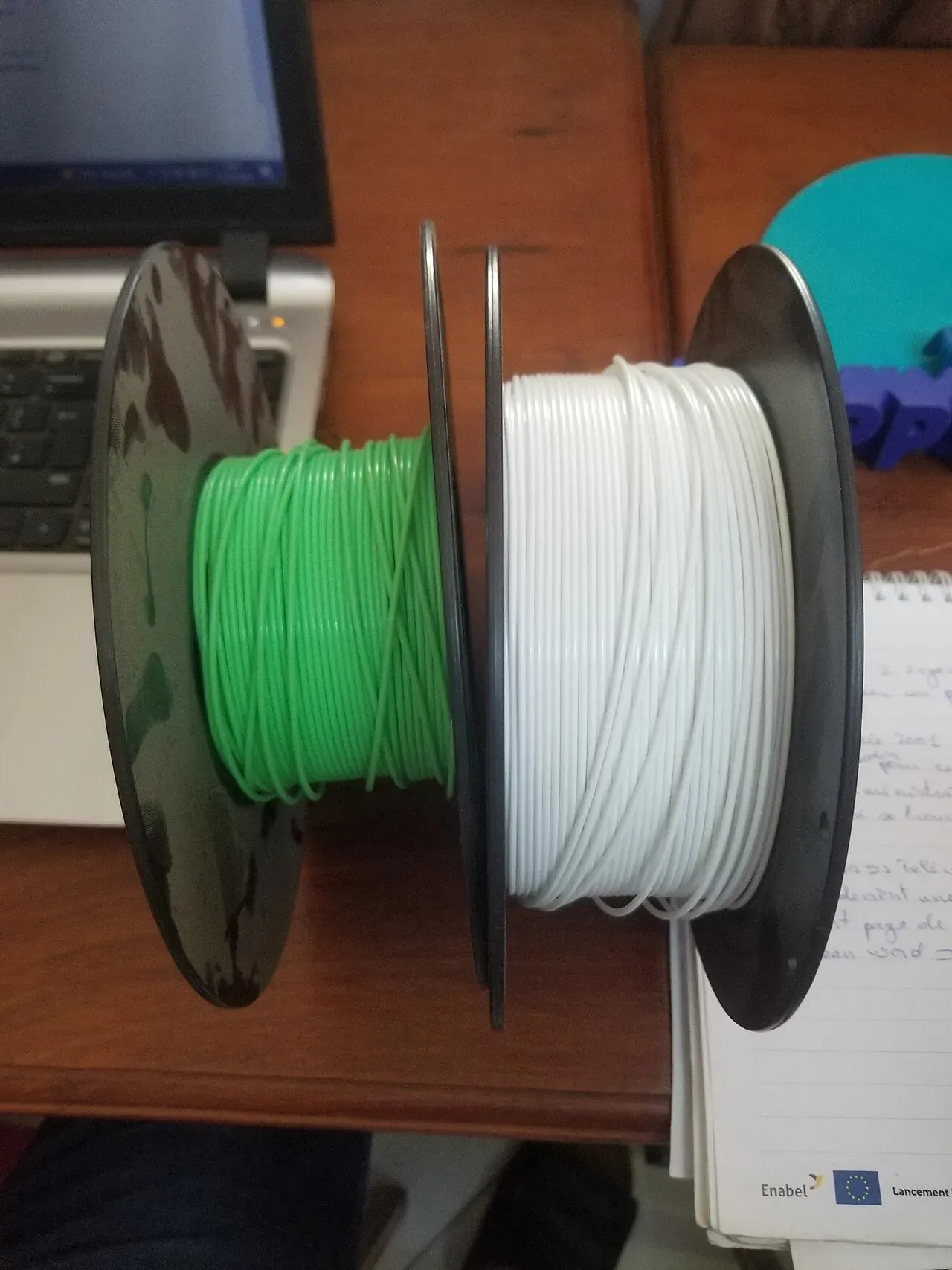 Green and white PLA filament spools side by side