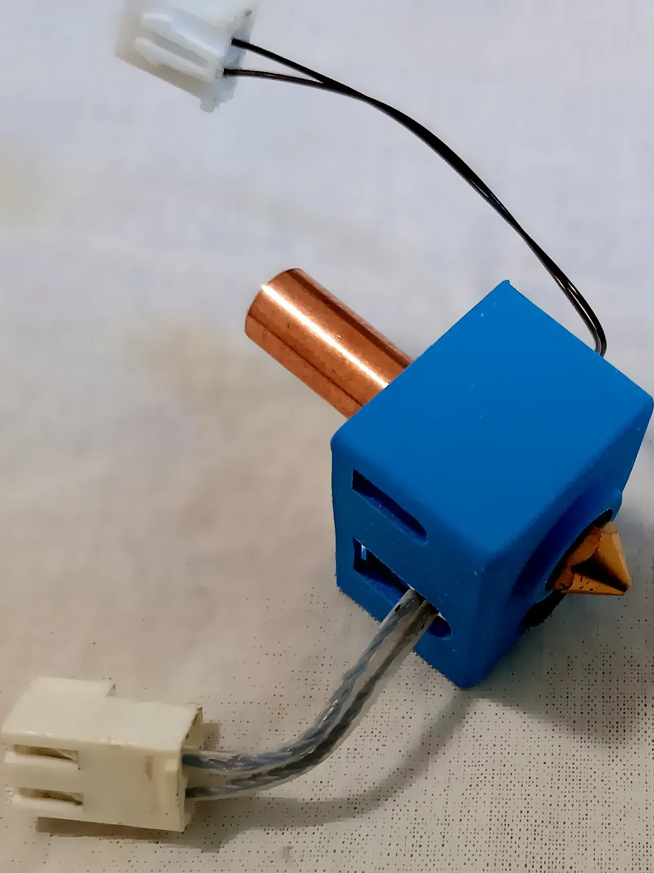 A blue silicone-wrapped heater block with a brass nozzle and heat break